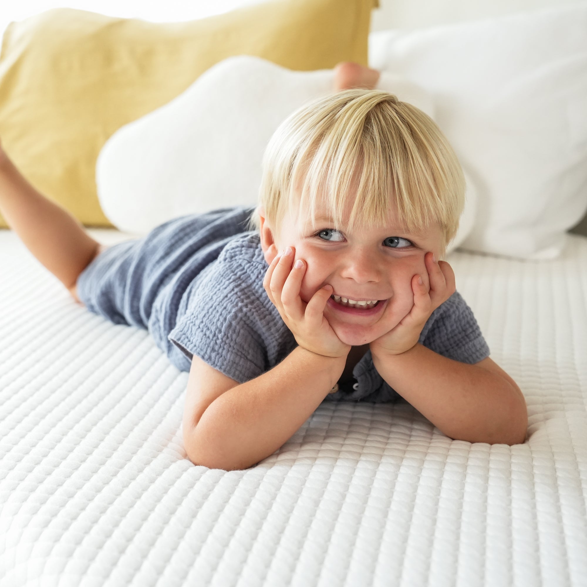 Child in green shirt and orange shorts lying on a textured white surface.