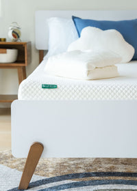 Memory foam mattress with white bedding and wooden bed frame in a modern bedroom.