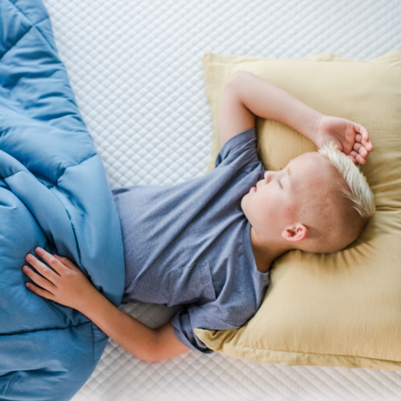 Child in green shirt and orange shorts lying on a textured white surface.