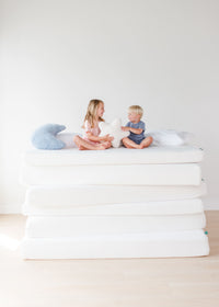Children sitting on stacked mattresses with star and moon pillows in a minimalist bedroom.