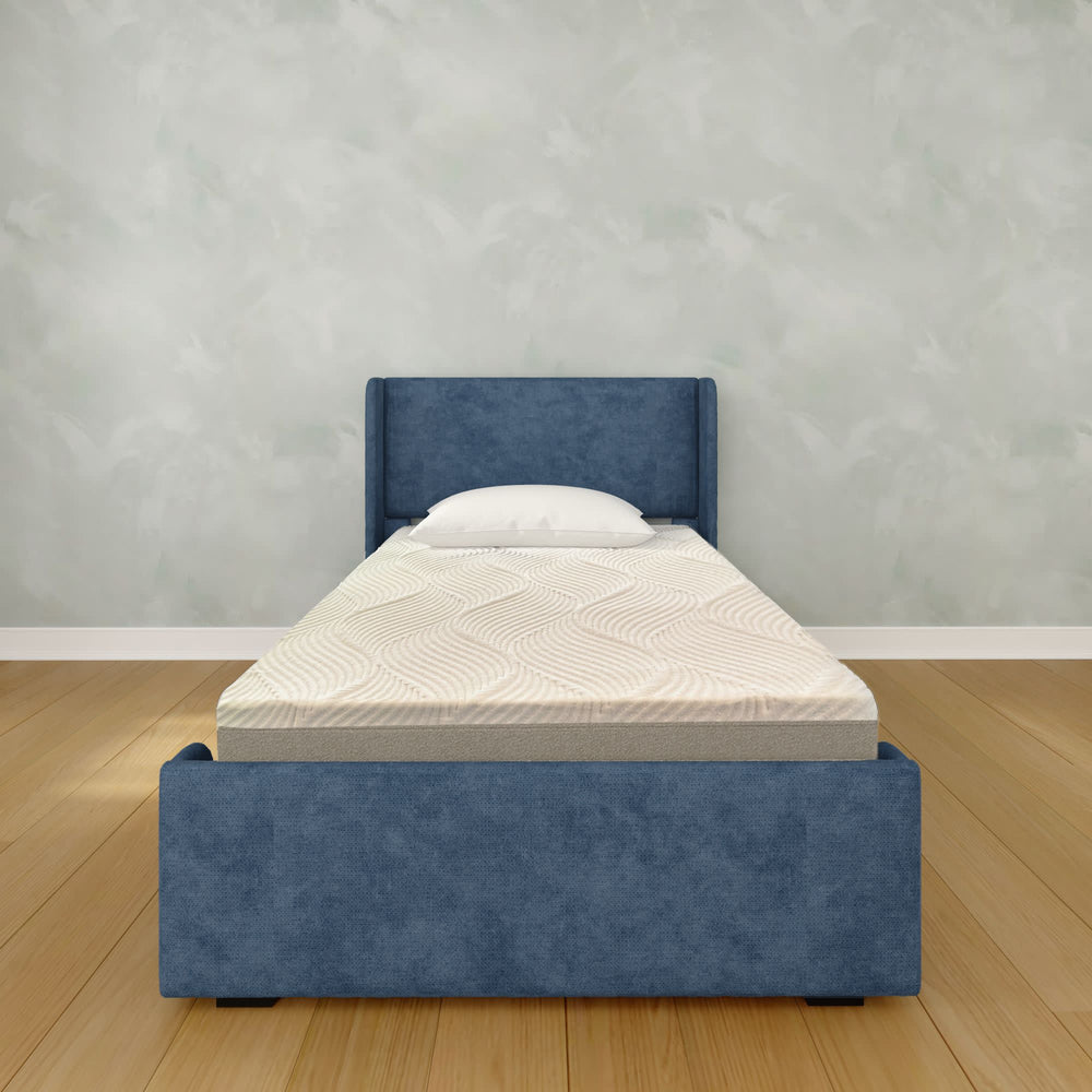 Single bed with blue fabric headboard and mattress in a minimalist bedroom setting.