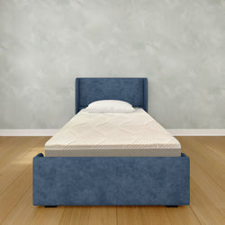Single bed with blue fabric headboard and mattress in a minimalist bedroom setting.