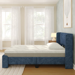 Blue upholstered bed with white mattress in a bright bedroom with sheer curtains.