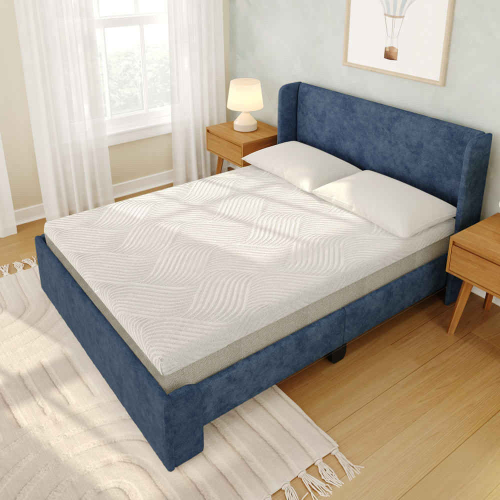 Modern bedroom with a plush blue upholstered bed frame, comfortable white mattress, and wooden nightstands, featuring natural light and cozy decor.