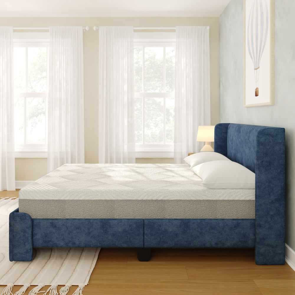 Modern bedroom featuring a comfortable blue upholstered bed with a mattress and pillows near large windows with sheer curtains.