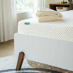 Memory foam mattress on modern bed frame with folded sheets in a bright bedroom.