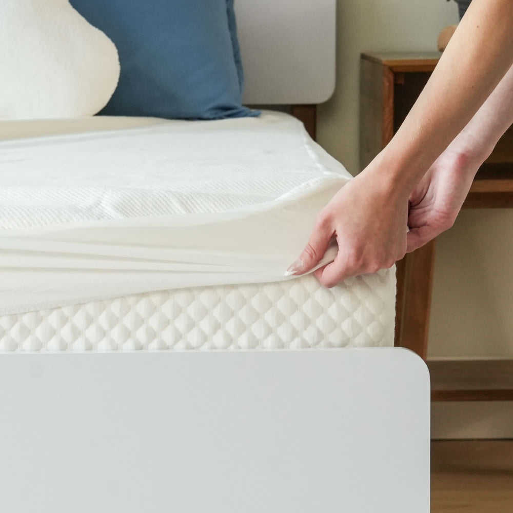 Person adjusting a fitted sheet on a bed with a comfortable mattress in a modern bedroom.
