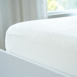 White memory foam mattress with checkered pattern on modern bed frame in a bright bedroom setting.
