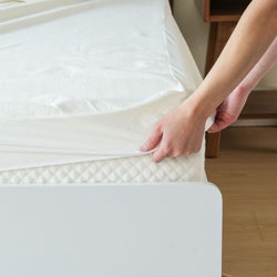 Person changing bed sheet on a comfortable mattress in a cozy bedroom setting