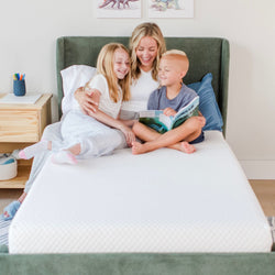 Family enjoying reading time on a comfortable bed with white bedding in a cozy bedroom setting.