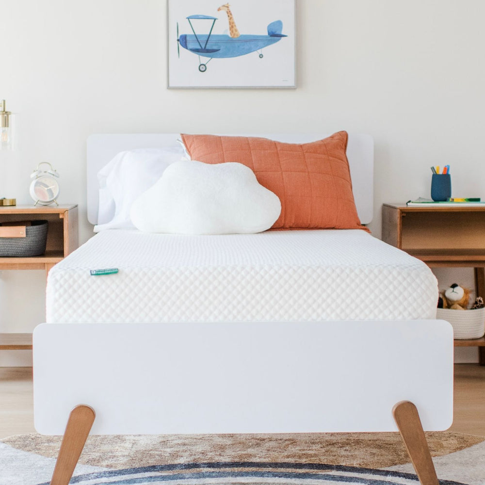 Modern kids' bedroom with a comfortable mattress, orange pillow, and cloud-shaped cushion.