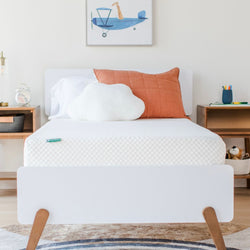 Modern kids' bedroom with a comfortable mattress, orange pillow, and cloud-shaped cushion.