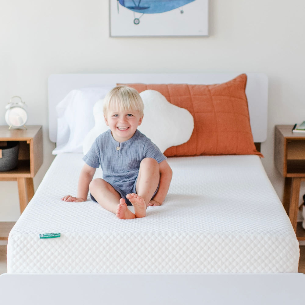Smiling child sitting on a comfortable, eco-friendly memory foam mattress in a cozy bedroom setting.