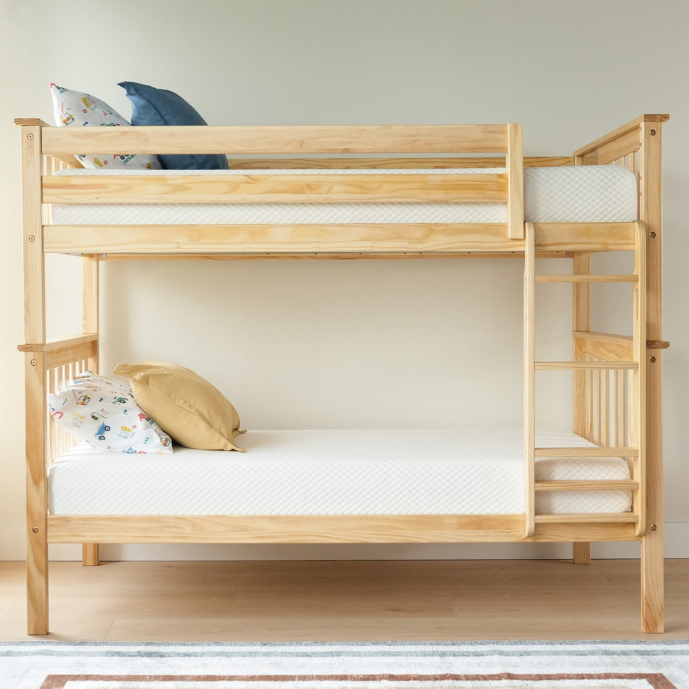 Light wood bunk bed with white mattresses and colorful pillows in a minimalist bedroom setting.