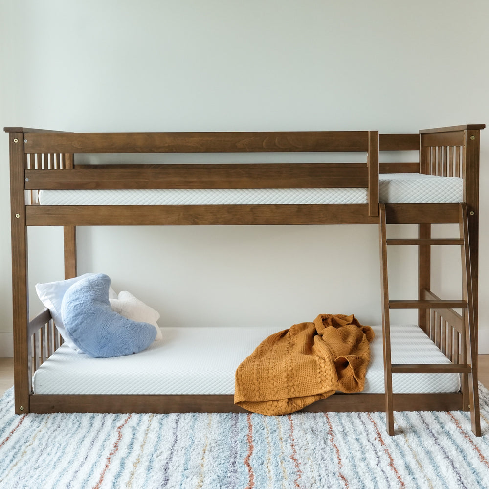 Wooden bunk bed with ladder, white mattresses, cozy orange blanket, and decorative pillows on a patterned rug in a children's bedroom.