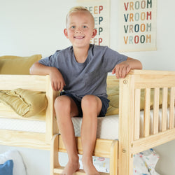 Child smiling while sitting on a cozy wooden bunk bed in a playful bedroom setting.