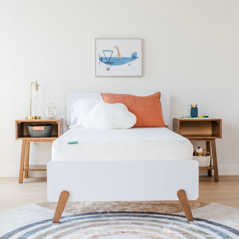 Modern bedroom with white bed, cloud pillow, orange cushion, and stylish wooden nightstands.
